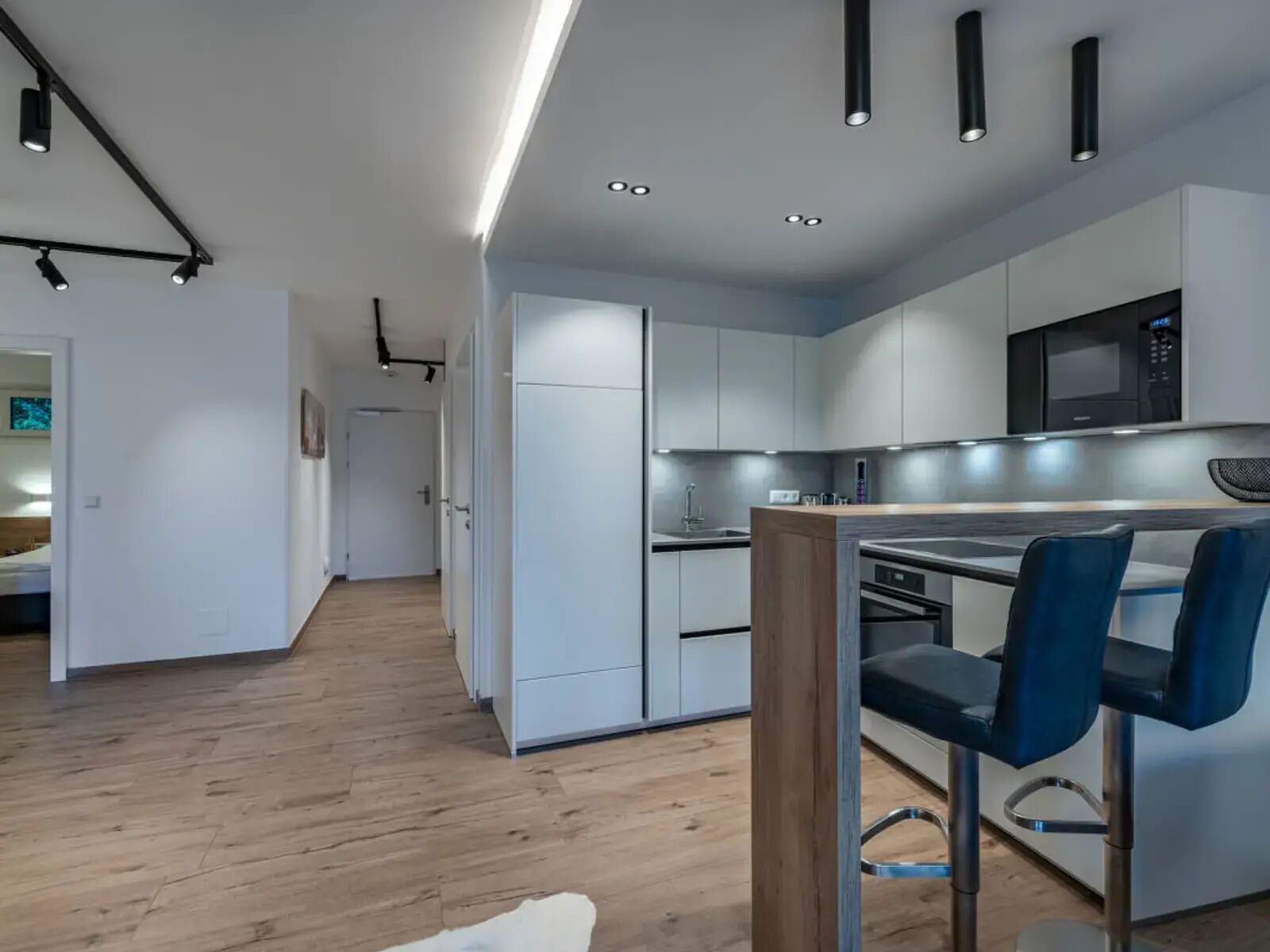A modern kitchen with white cabinets, a microwave, and a bar area with blue chairs.