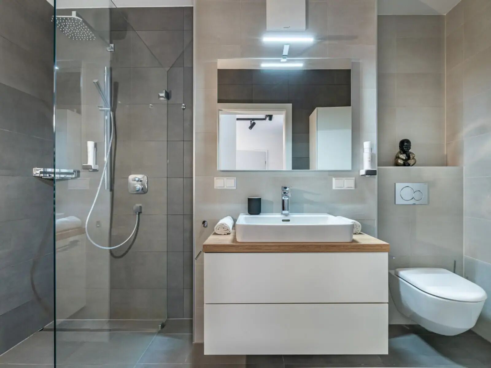 A modern bathroom with a glass shower enclosure, a white vanity with a wooden countertop, a large mirror, and a toilet.