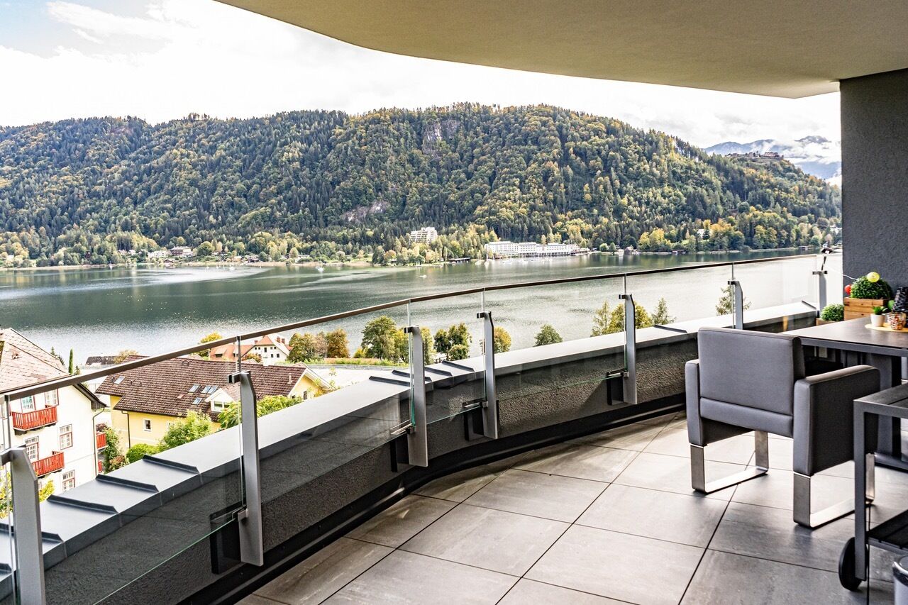 A balcony with a view of a lake and forested hills.