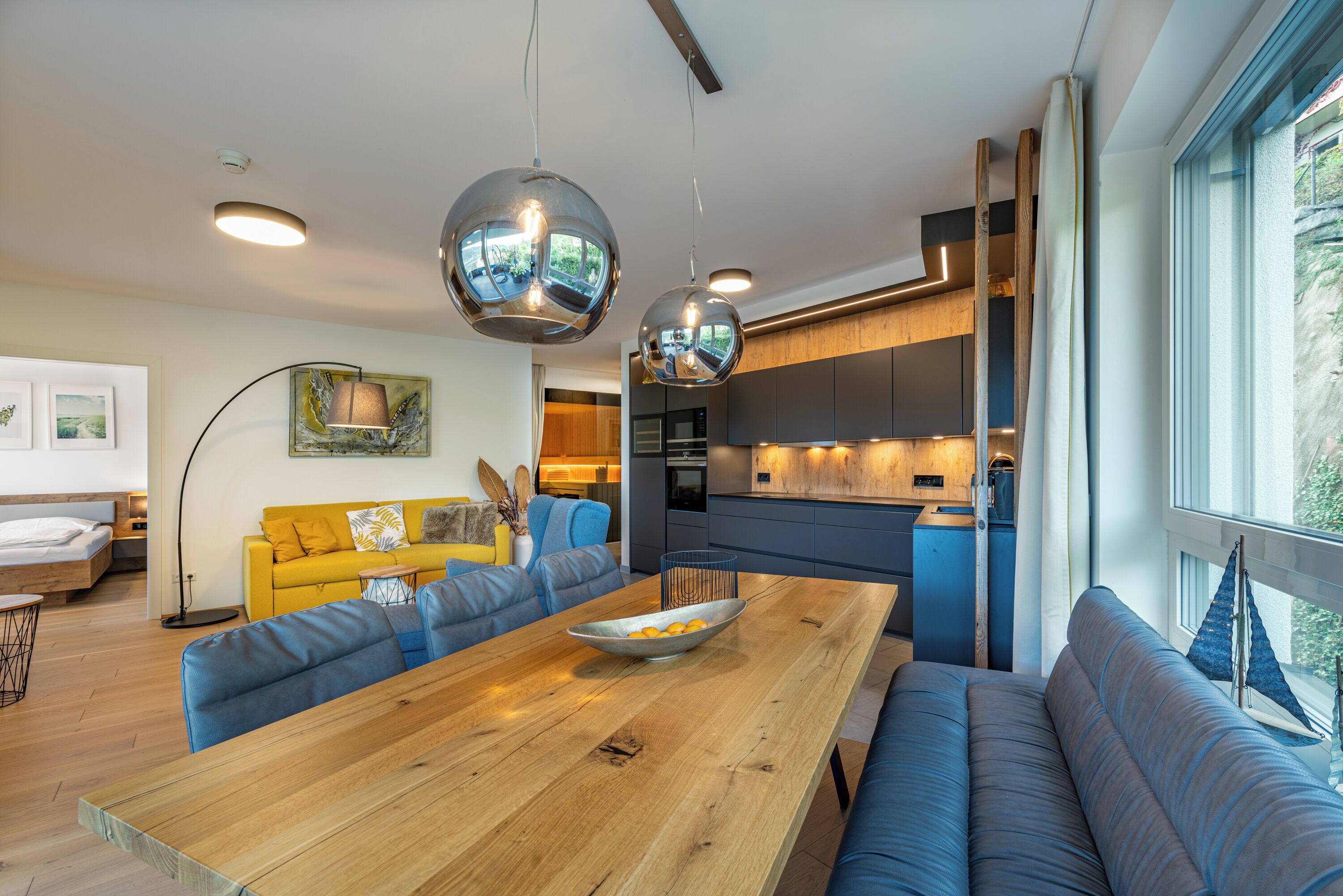 A modern kitchen with a dining area, a sofa, and a large window.