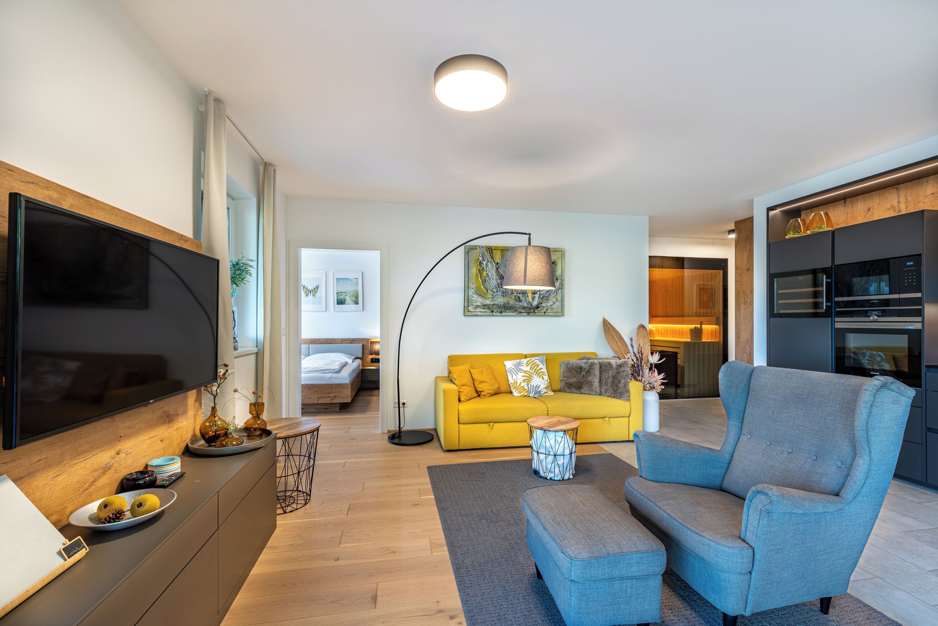 A modern living room with a flat-screen TV, a sofa, a coffee table, and a dining area with a microwave.
