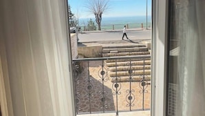 Ein Zimmer mit einem großen Fenster, Blick auf einen Balkon mit Geländer und einem klaren Himmel.