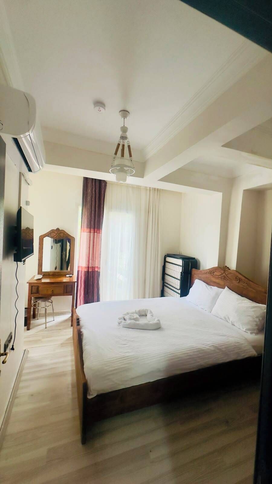 Una habitación de hotel con cama, escritorio con espejo, una silla, unidad de aire acondicionado y ventilador de techo.