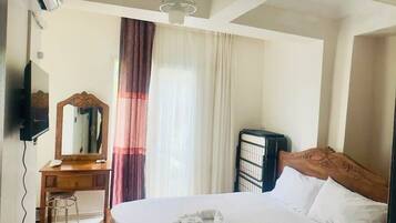 Una habitación de hotel con cama, escritorio con espejo, una silla, unidad de aire acondicionado y ventilador de techo.