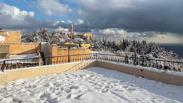 Ein mit Schnee bedecktes Dach, ein klarer Himmel, eine entfernte Ansicht eines historischen Gebäudes und ein Metallgeländer.