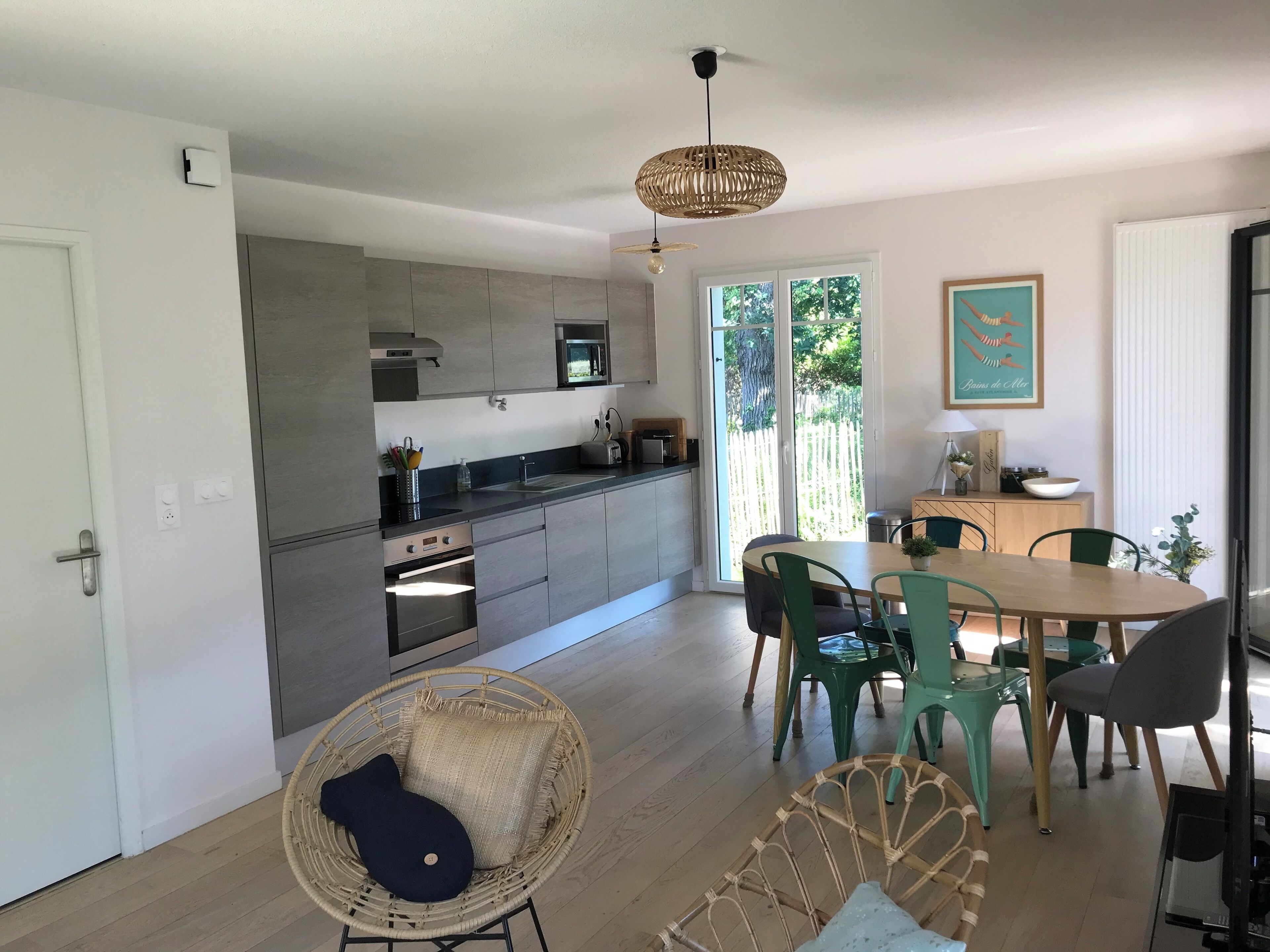 Een moderne keuken met een eethoek, rieten stoelen en uitzicht door de glazen deur.