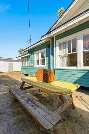 A house with a green exterior, white trim, and a wooden bench with a checkered tablecloth.