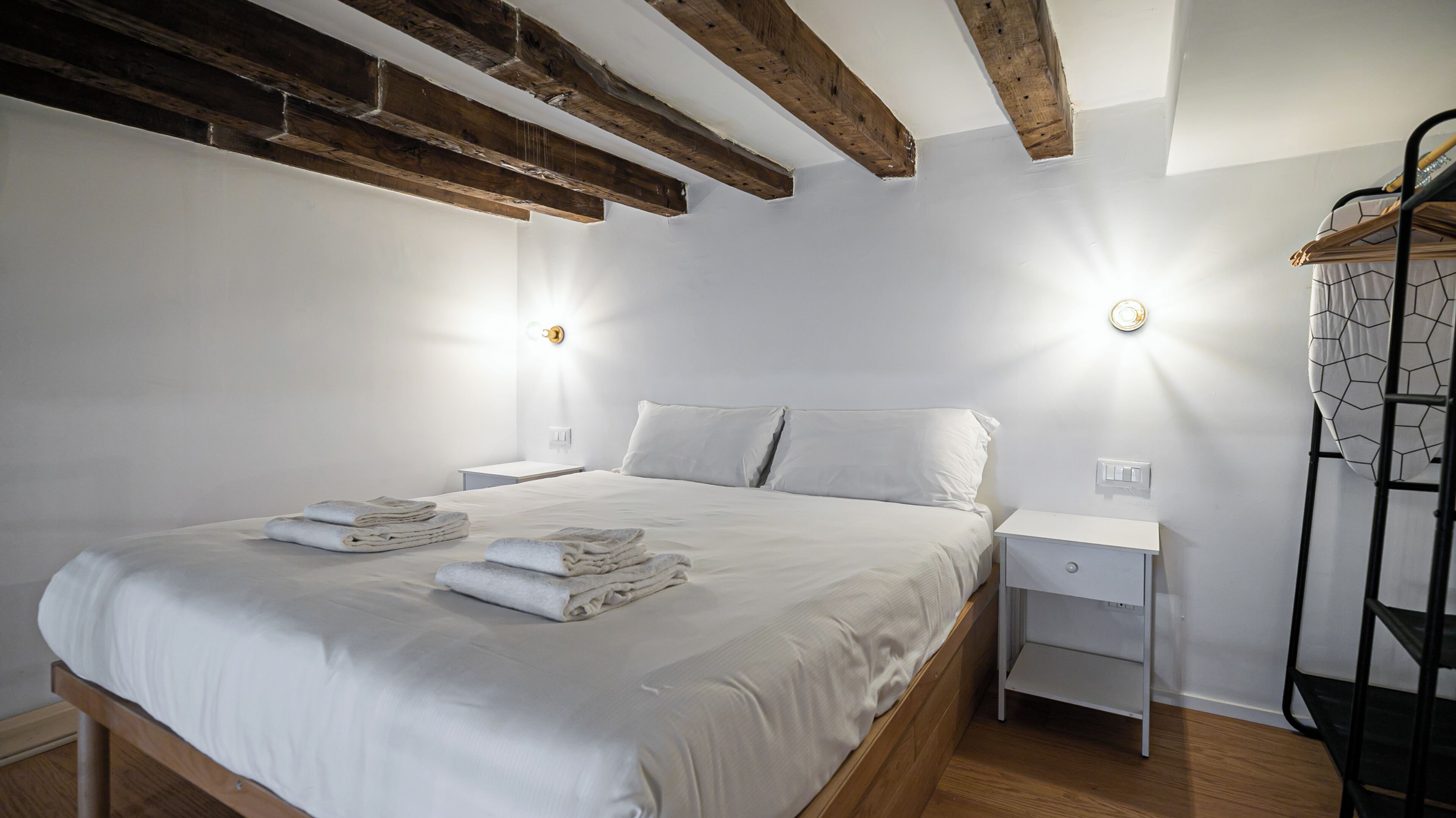 A bedroom with a bed, two bedside tables, a wooden floor, and exposed wooden beams on the ceiling.