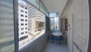 A balcony with a table and chairs, a view of a building, and a tiled wall. - Beachfront apartment - Praia Grande (Aviação) with side view of the sea. (Praia Grande)