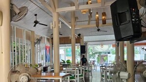 A restaurant interior with high ceilings, ceiling fans, and a stage with a sound system. - Fishermans Village Samui Yoga Retreat (Koh Samui)