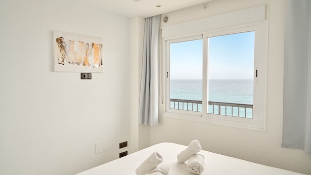 Een hotelkamer met een bed, een raam met uitzicht op zee en een schilderij aan de muur.