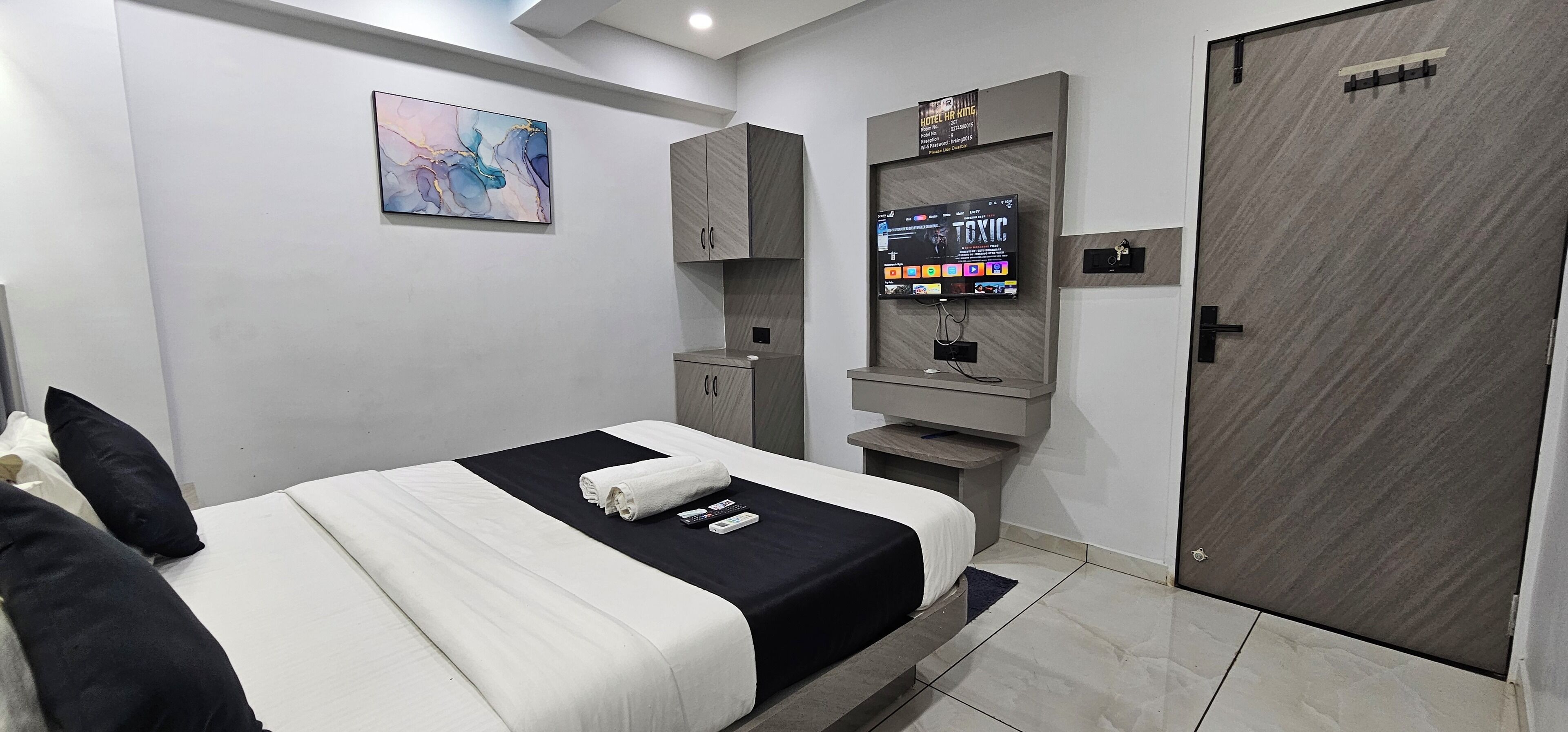Een moderne hotelkamer met een bed, een televisie, een kledingkast en een schilderij aan de muur.