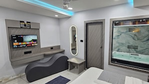 Habitación de hotel moderna con televisión, espejo grande, bañera de mármol y zona de estar.