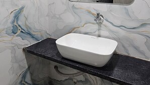 Un baño con pared de mármol, lavamanos blanco y encimera negra.