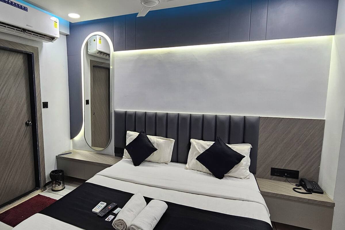 Una habitación de hotel moderna con cama, mesita de noche, espejo y aire acondicionado integrado.