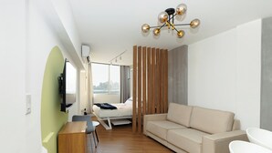 Un salón moderno con sofá, televisor montado en la pared, separador de madera y vista a la ciudad a través de amplias ventanas.