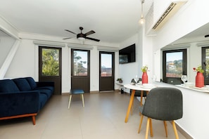 Ein modernes Wohnzimmer mit einer Couch, einem Esstisch, Stühlen, einem Deckenventilator und großen Fenstern.