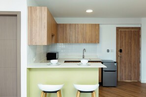 A modern kitchen with wooden cabinets, a white countertop, two white bar stools, a sink, and a refrigerator. - Located in the heart of Casco Viejo’s nightlife 🎶🌃<br>Steps from bars and nightclubs, perfect for those who want a lively vibe 🍸🕺<br>There is nighttime noise due to the nightclub area 🔊✨ (Casco viejo)