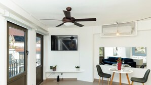 Ein modernes Wohnzimmer mit Deckenventilator, einem Wand-Fernseher, einem Esstisch mit Stühlen und einem Balkon mit Blick.