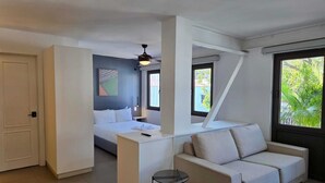 Ein modernes Hotelzimmer mit Bett, Sofa, kleinem Tisch, Deckenventilator und Fenster mit Blick auf Grünflächen.