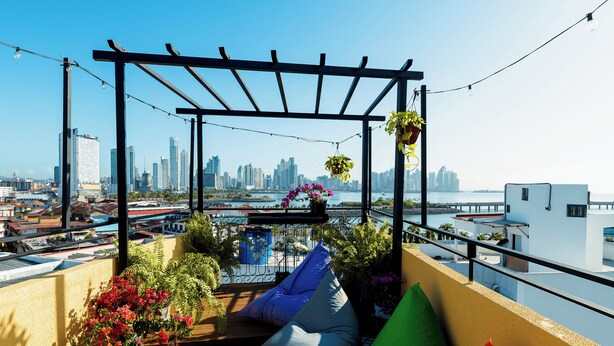 Eine Dachterrasse mit Blick auf die Stadtlandschaft, einer Pergola und Kübelpflanzen.