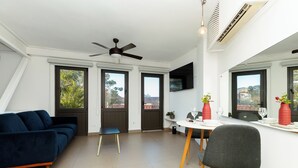 Ein modernes Wohnzimmer mit einer Couch, einem Esstisch, Stühlen, einem Deckenventilator und großen Fenstern.
