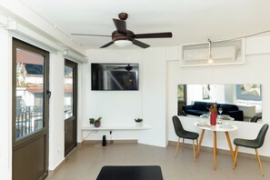 Ein modernes Wohnzimmer mit Deckenventilator, einem Wand-Fernseher, einem Esstisch mit Stühlen und einem Balkon mit Blick.
