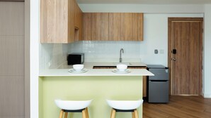 Une cuisine moderne avec des meubles en bois, un plan de travail blanc, deux tabourets de bar blancs, un évier et un réfrigérateur.