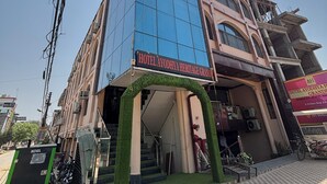Un hôtel doté d’une façade moderne en verre, d’une enseigne indiquant « Hôtel Ayodhya Heritage Grande », et d’une arche verte à l’entrée.