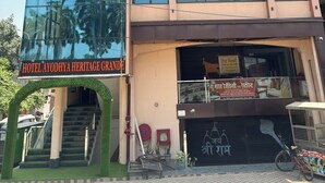 Un hôtel à plusieurs étages doté d’une grande façade en verre, d’une enseigne indiquant « Hôtel Ayodhya Heritage Grande » et d’un escalier menant à l’entrée.