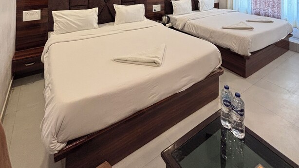Une chambre d’hôtel avec deux lits, une tête de lit en bois, un ventilateur de plafond et une fenêtre avec des rideaux.