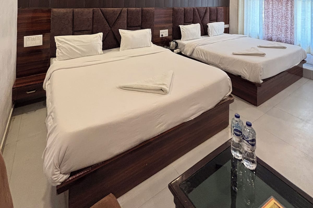 Een hotelkamer met twee bedden, een houten hoofdbord, een plafondventilator en een raam met gordijnen.