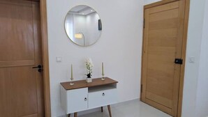 A room with a wooden door, a white cabinet with drawers, a round mirror, and a small vase with flowers. - Modern & Stylish 1BR Apt | Cidadela | Ground Floor (Praia)