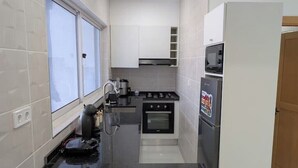 A compact kitchen with white cabinets, a stove, oven, microwave, and a coffee maker. - Modern & Stylish 1BR Apt | Cidadela | Ground Floor (Praia)