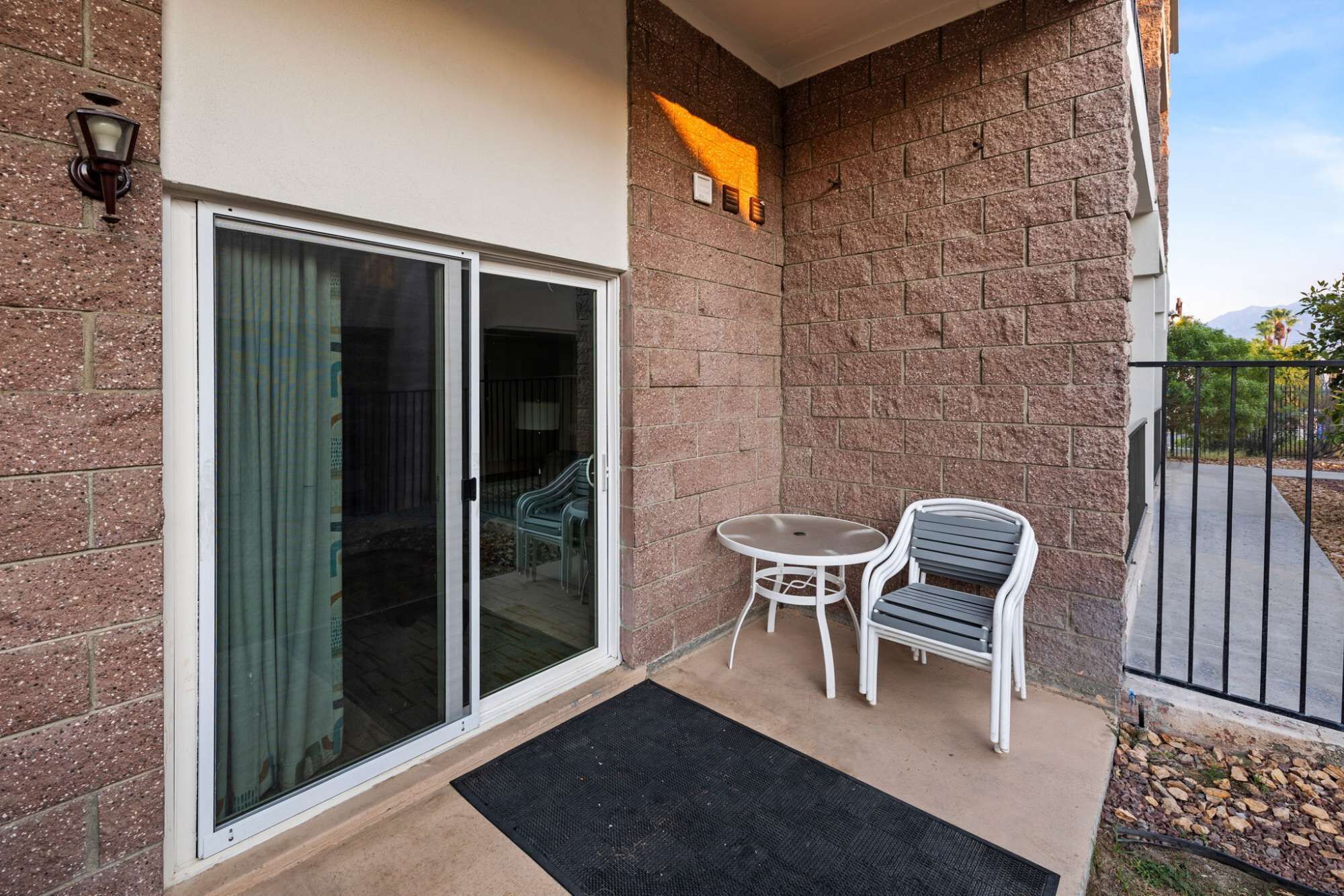 A balcony with a sliding glass door, a small table with two chairs, and a black doormat.