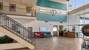 Eine geräumige Lobby mit einer Treppe, einem roten Sofa, einem Empfangsbereich und einem großen Fenster.