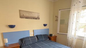 A bedroom with a bed, bedside tables, a nightstand, a wall-mounted lamp, a picture, and a window with curtains. - Estartit Costa Brava. En bord de MER. Bel appartement avec vue sur la mer (L’Estartit (or Estartit))