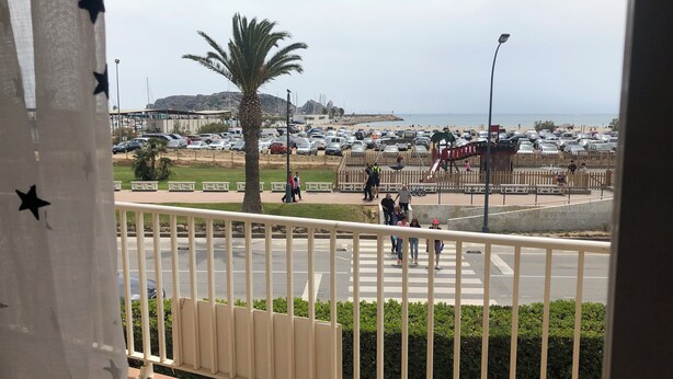 A balcony with a view of a busy street, a playground, and a beach in the distance. - Estartit Costa Brava. En bord de MER. Bel appartement avec vue sur la mer (L’Estartit (or Estartit))