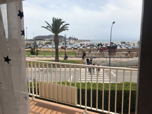Uma varanda com vista para uma rua movimentada, um parquinho e uma praia ao longe.