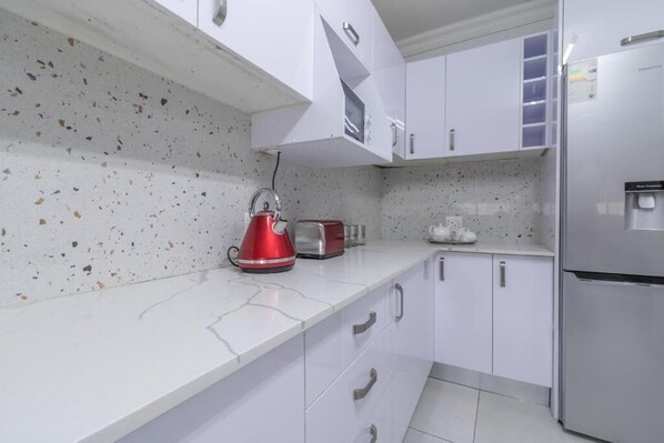 Una cocina con armarios blancos, un refrigerador de acero inoxidable, un hervidor rojo y una tostadora.