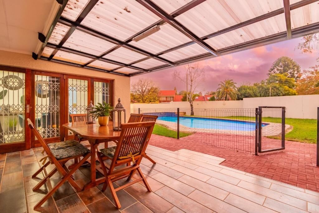 A covered patio with a pool, wooden furniture, and a view of the surrounding area.