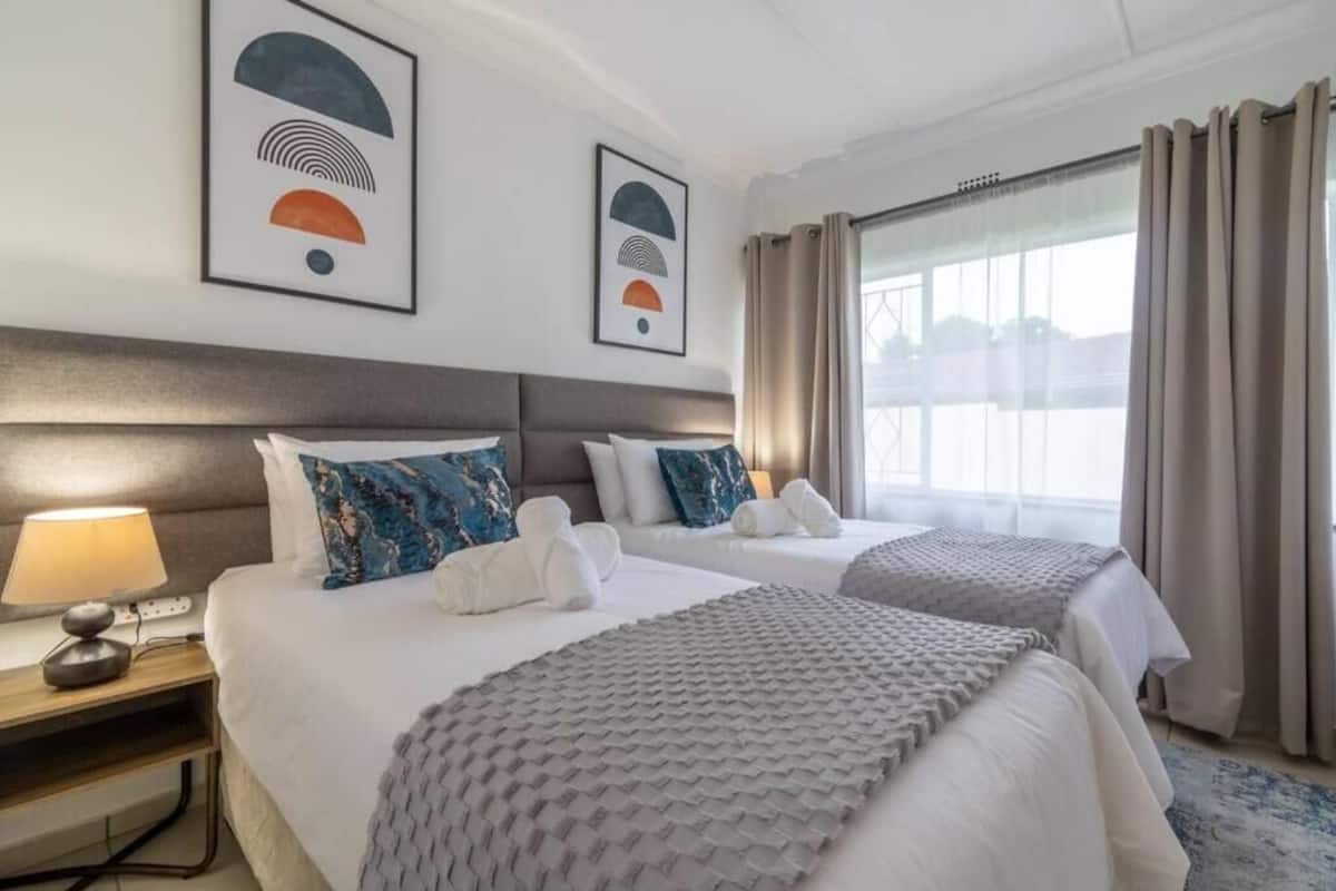 A hotel room with two beds, a nightstand with a lamp, and artwork on the walls.