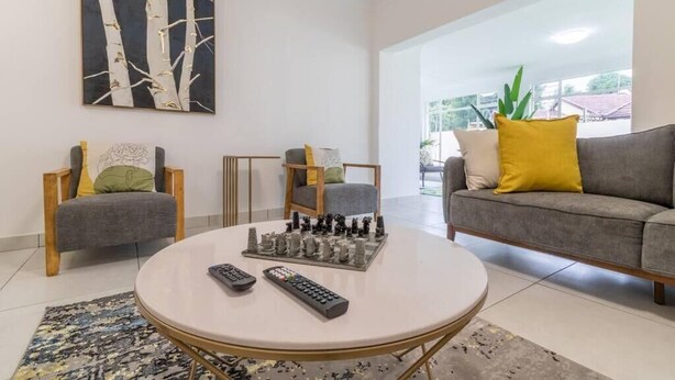 A modern living room with a round coffee table, two armchairs, a sofa, and a chessboard. - Greencroft Villa (Kempton Park)