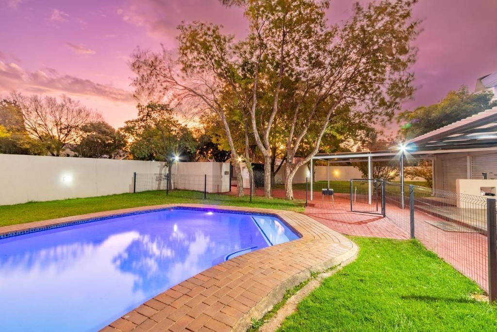 A swimming pool with a brick border, surrounded by a grassy area and trees.