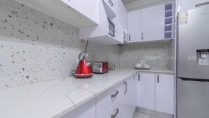 A modern kitchen with white cabinets, a stainless steel refrigerator, a red kettle, and a toaster. - Greencroft Villa (Kempton Park)