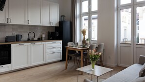 Une cuisine moderne avec des meubles blancs, un coin repas comprenant une table et des chaises, et une fenêtre donnant sur des immeubles.