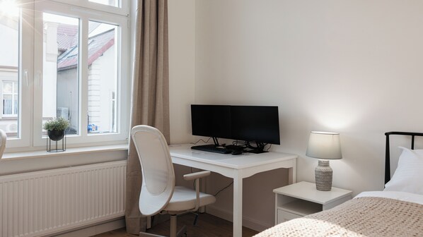Una habitación de hotel con un escritorio blanco, una computadora, una silla, una lámpara y una cama.