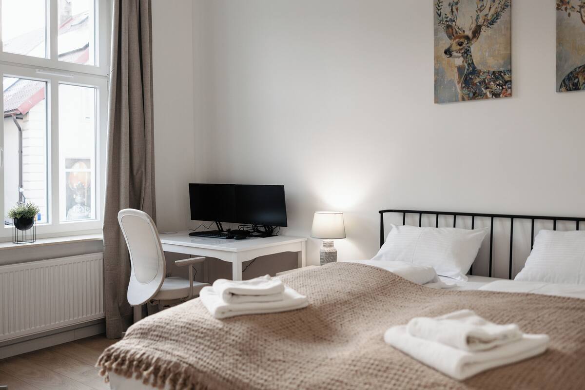 Una habitación de hotel con cama, escritorio con computadora, silla y una obra de arte en la pared.