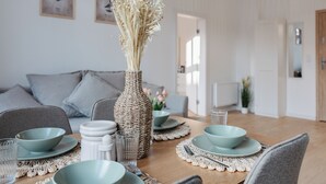 Une table à manger dressée avec des bols, des assiettes et un vase contenant des fleurs séchées.