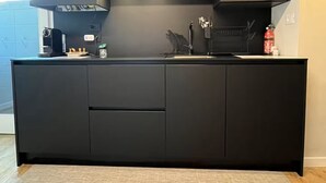 A modern kitchen with dark cabinetry, a built-in oven, and a stainless steel range hood. - Piccola Perla sul canale (Venezia)